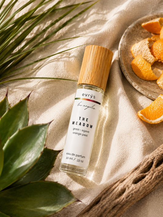 Oil roller bottle labeled 'The Meadow' with orange peels and green leaves on a beige fabric background