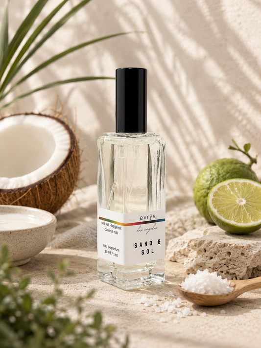 Perfume bottle of 'evrys Sand & Sol' with a black cap on a neutral background with coconut, lime, and salt.
