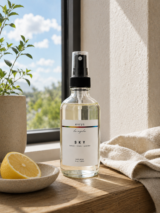 Room spray bottle labeled 'SKY' on a wooden surface with a window and plant in the background