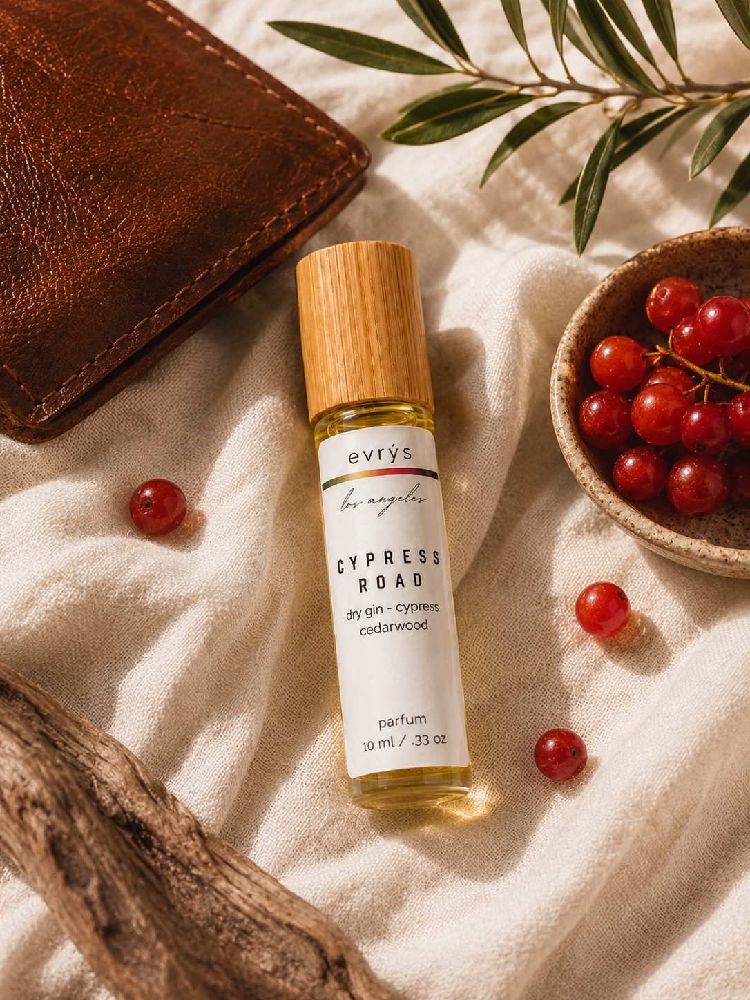 evrys Cypress Road oil roller bottle on a textured surface with berries and a wallet.