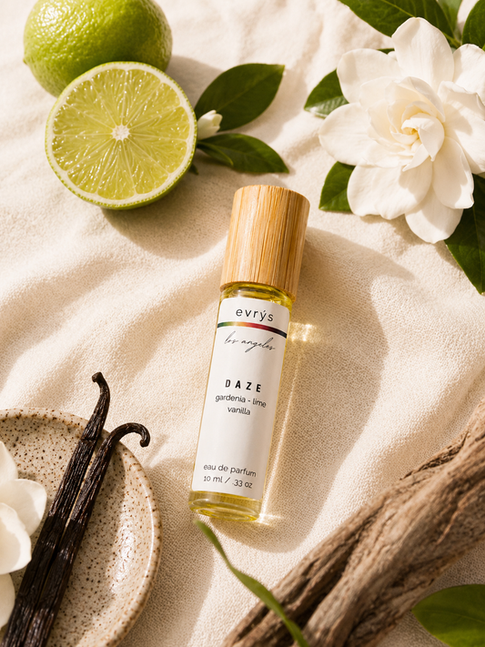 evrys Daze oil roller bottle with vanilla beans, limes, and flowers on a light background