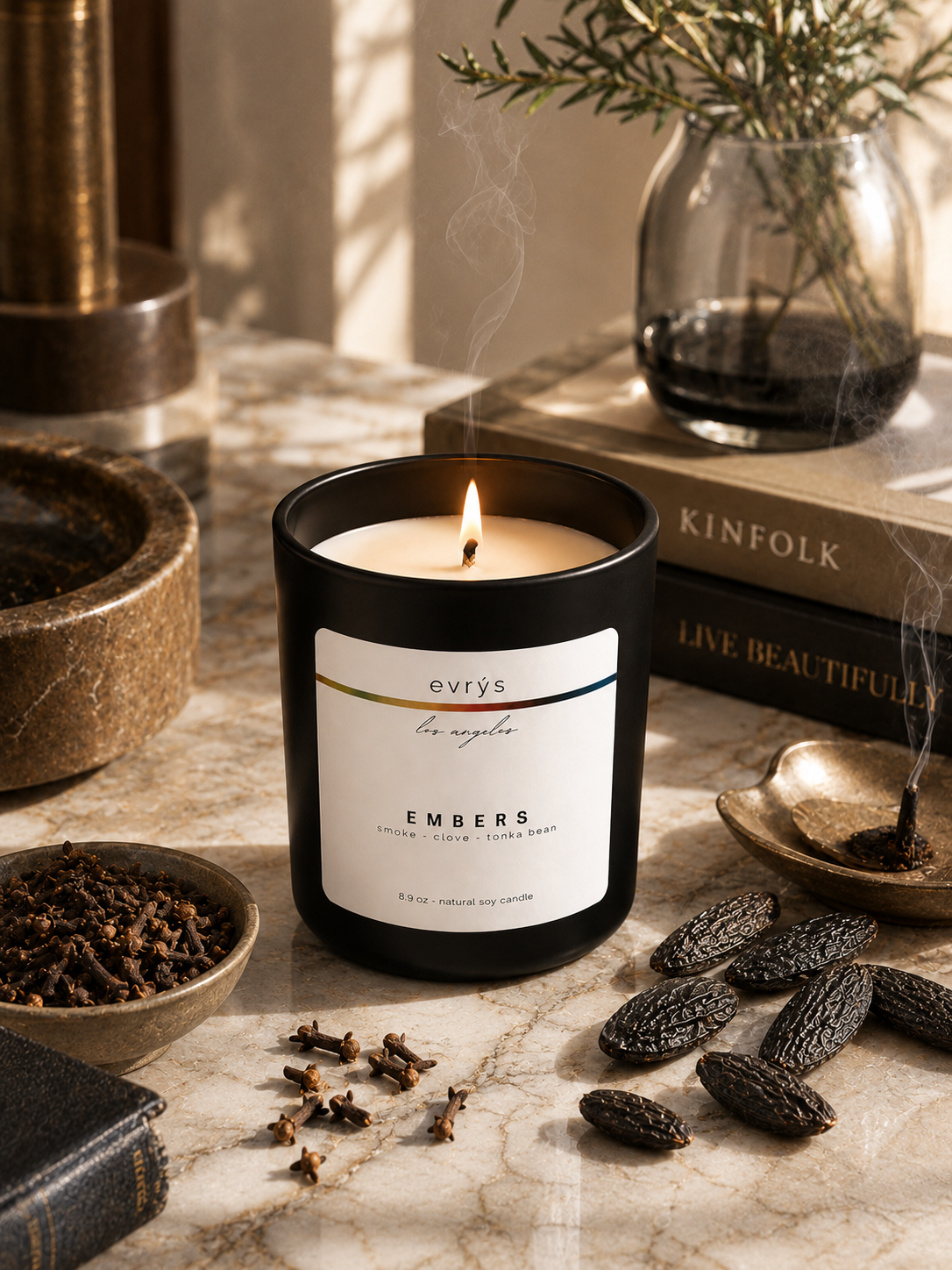 evrys candle labeled 'Embers' on a marble surface with books and decorative items.