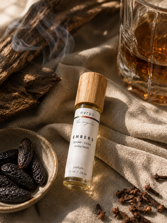 evrys Embers oil roller bottle with dried fruits and a glass of whiskey on a textured surface