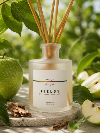 Reed diffuser labeled 'FIELDS' by evrys with green apples and leaves in the background