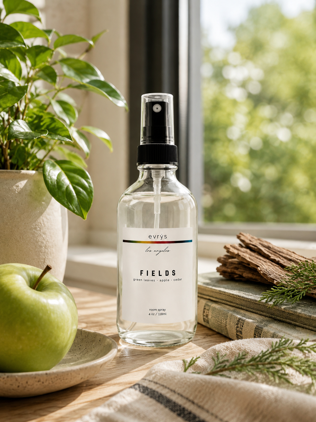 Room spray bottle labeled 'FIELDS' on a wooden surface with an apple and plant in the background