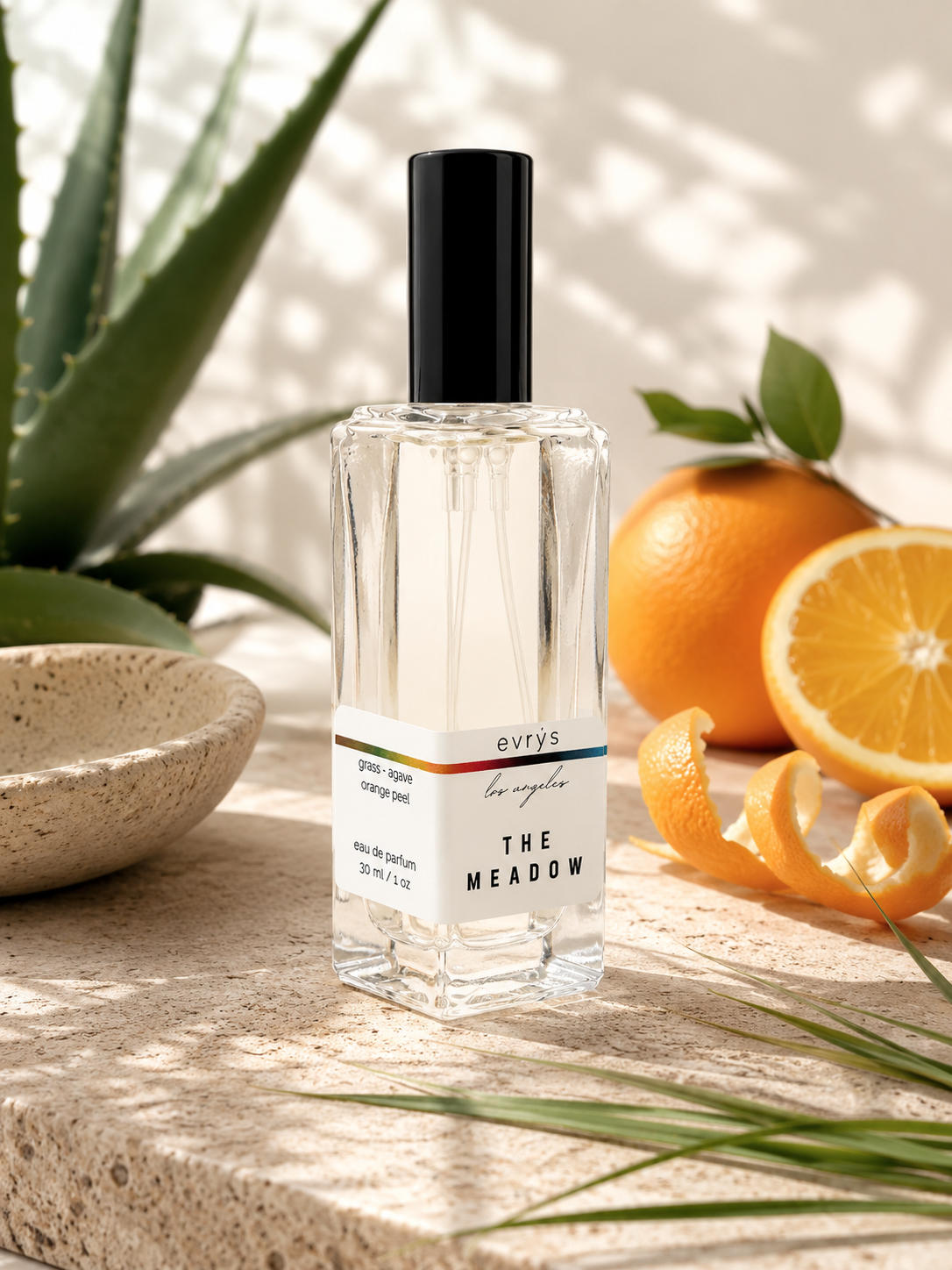 Perfume bottle labeled 'The Meadow' on a stone surface with oranges and a plant.