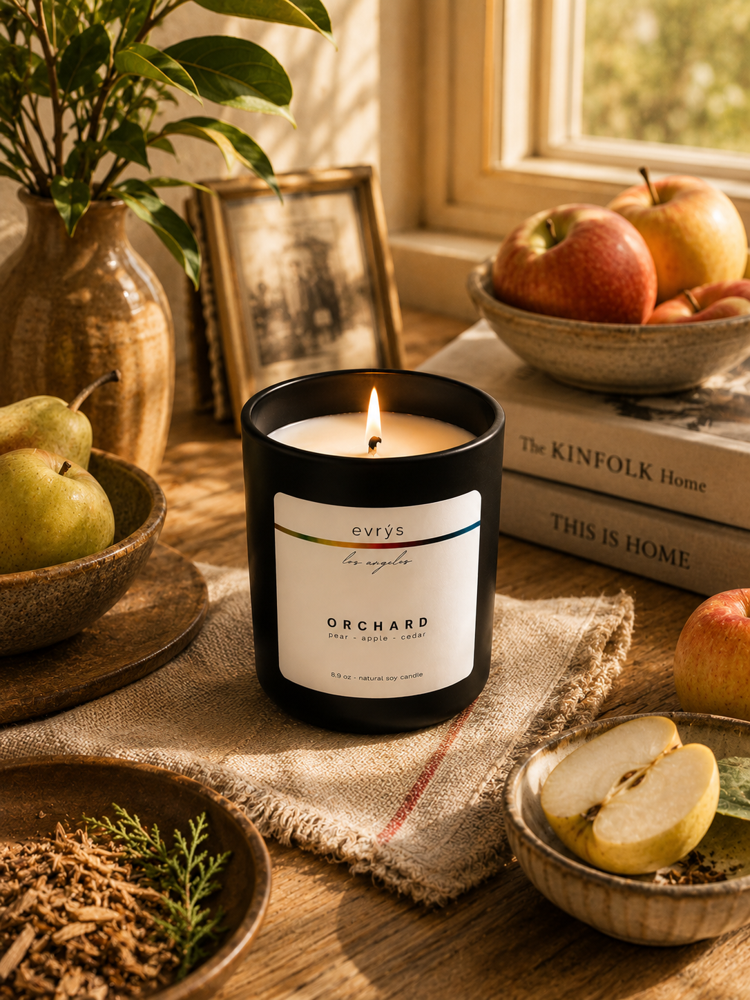 Candle labeled 'Orchard' by evrys on a wooden surface with apples and books in the background.
