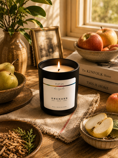 Candle labeled 'Orchard' by evrys on a wooden surface with apples and books in the background.