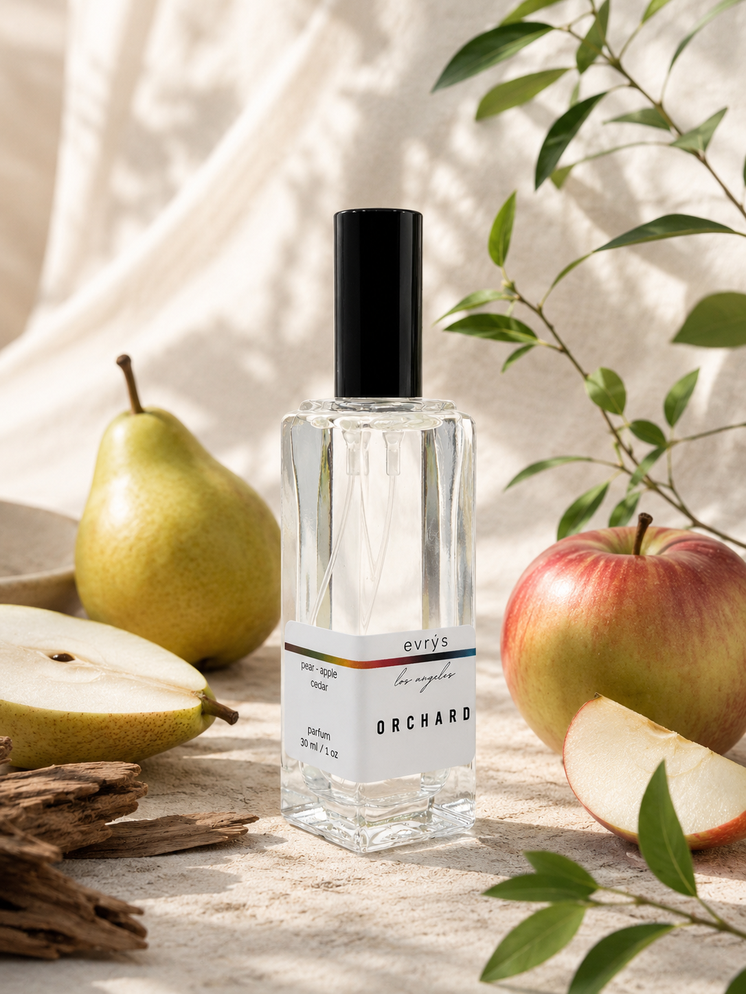 Perfume bottle labeled 'Orchard' by evry's on a wooden surface with pears and apples, and cedar.