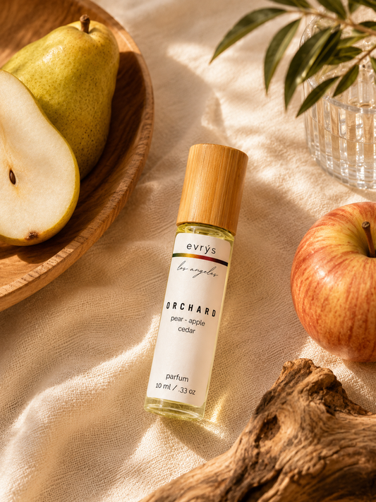 evrys Orchard oil roller bottle on a textured surface with pears and an apple.