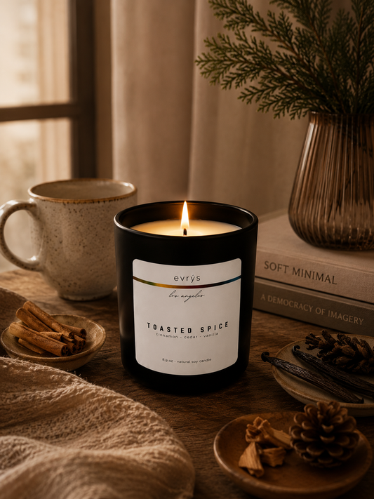 Candle labeled 'Toasted Spice' on a table with a mug, books, and decorative items.