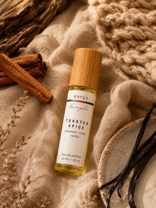 evrys Toasted Spice oil roller bottle with cinnamon sticks and vanilla beans on a textured fabric background